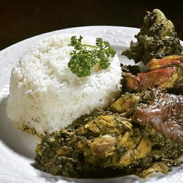 African dish with white rice, green herbs, and meat in a dark sauce on a white plate.