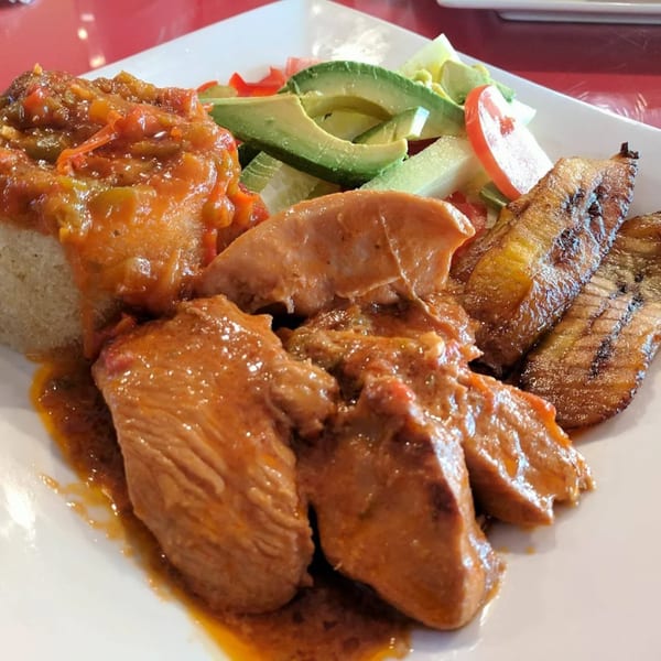 African dish with chicken in sauce, rice, fried plantains, and a side salad with avocado.