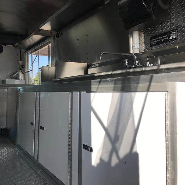 Interior of a Kendejah Restaurant food truck with stainless steel counters, sinks, and storage units.