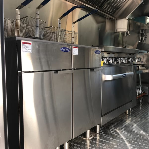 A clean, stainless steel commercial kitchen with fryers, a stove, and diamond plate flooring.