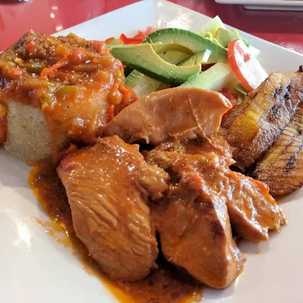 African chicken and rice dish with plantains and a side salad on a white plate.