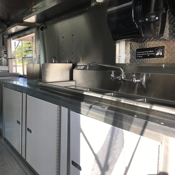 Interior of a Kendejah Restaurant food truck with stainless steel sinks, counters, and storage cabinets.